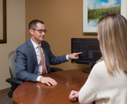 man in suit pointing at computer screen sitting across from woman